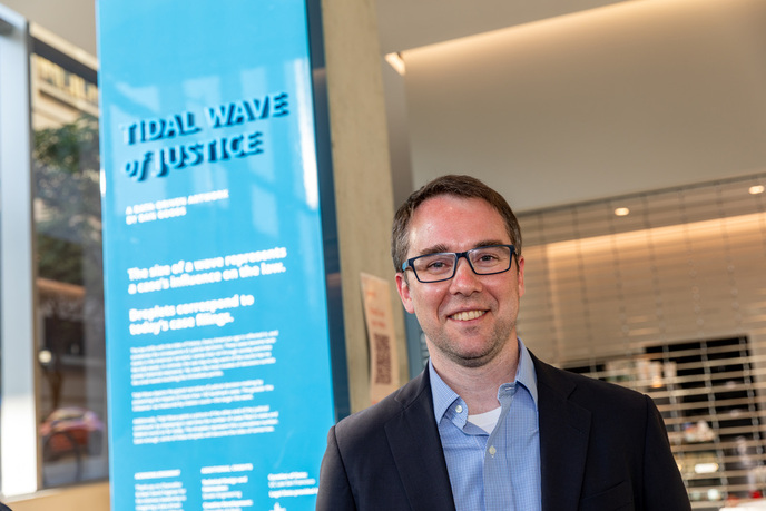 A man standing in front of the Tidal Wave of Justice informational sign at the opening event.