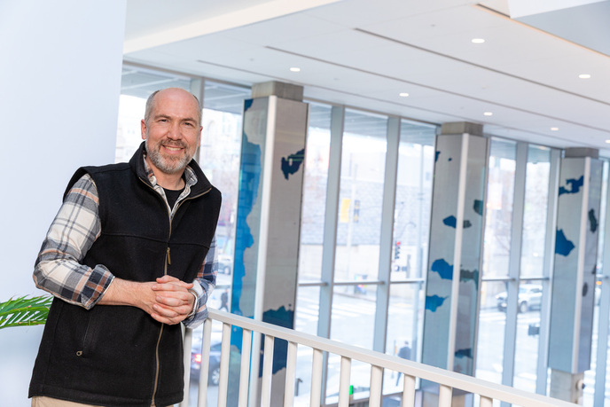 Artist Dan Goods standing in the atrium with the Tidal Wave of Justice installation visible on the pillars behind him.