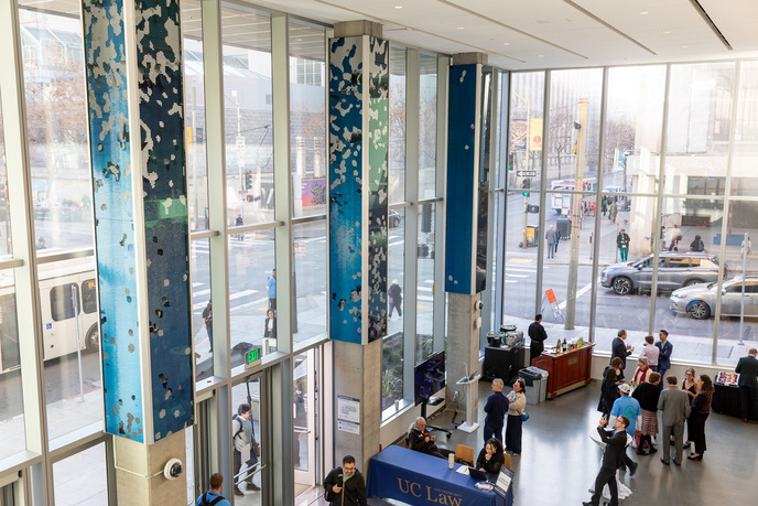 The Tidal Wave of Justice installation covering three massive pillars in the atrium of UC Law SF's newest building, with attendees gathered below during the opening event.